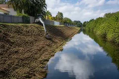 Residential drainage canal in Pembroke Pines with one bank freshly mowed to the waterline and the far bank still overgrown