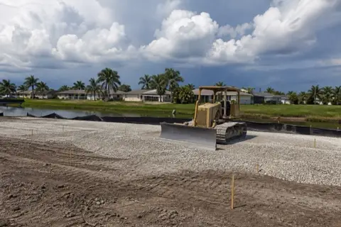 Small dozer spreading pale limerock across a cleared homesite pad in western Pembroke Pines with grade stakes set