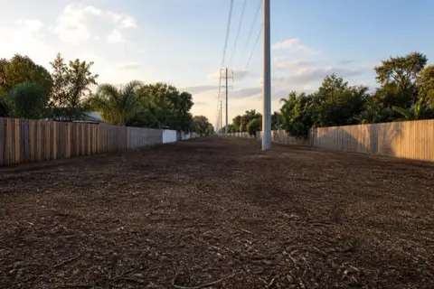 Long mulched utility easement running between backyard fences in Pembroke Pines with concrete power poles